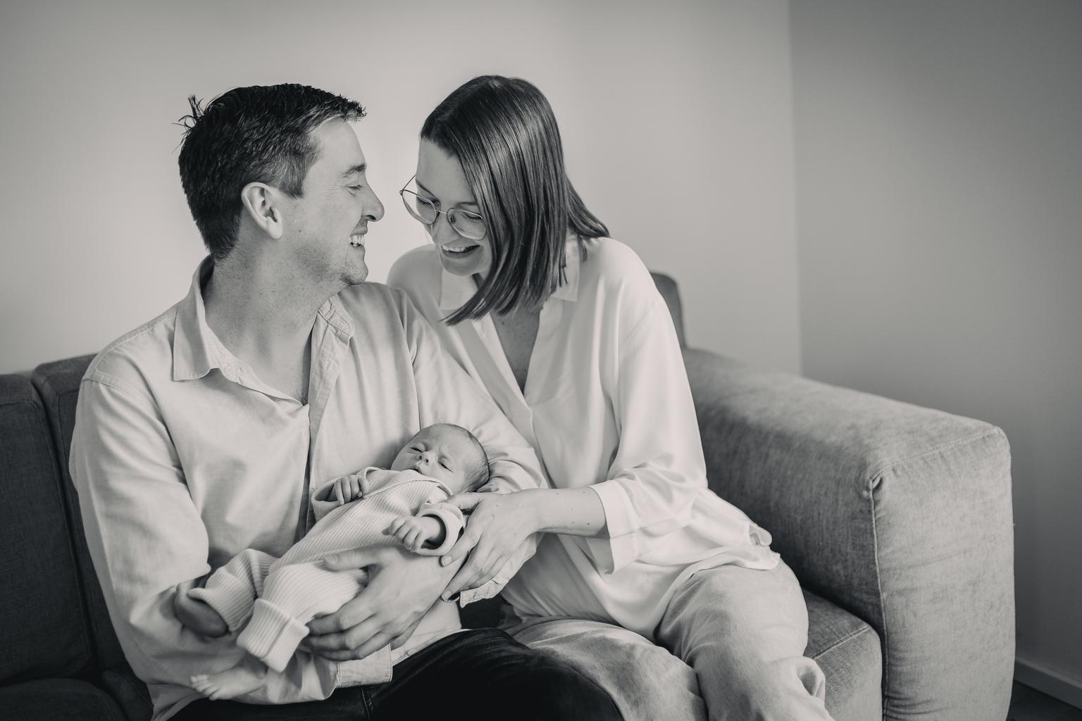 Schwarz-weiß Bild eines Paares das auf einer Couch sitzt und ein Baby im Arm hält.