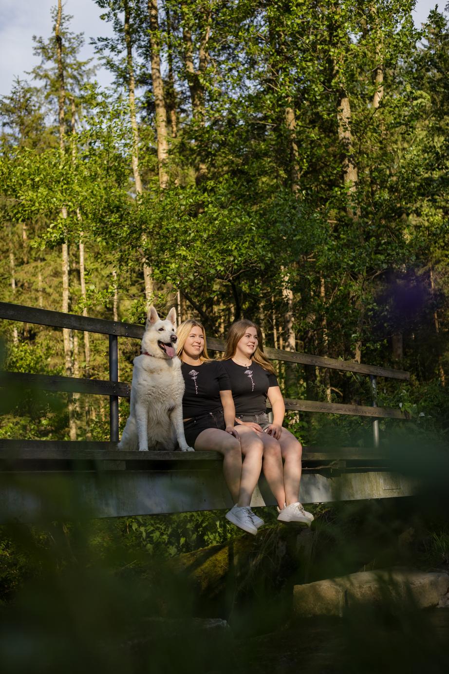 Zwei Frauen mit Hund sitzen auf einer Brücke.